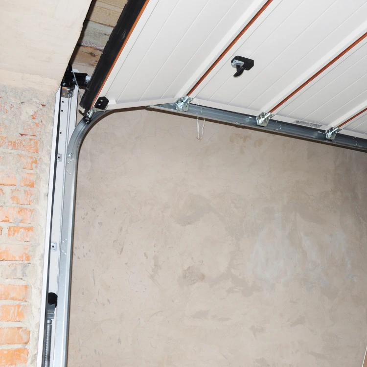 Upper section of a white garage door in a brick garage, showing the curved metal track, rollers, and inner components.
