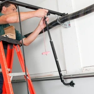 Garage door technician on a ladder working on the overhead opener's belt drive and emergency release mechanism