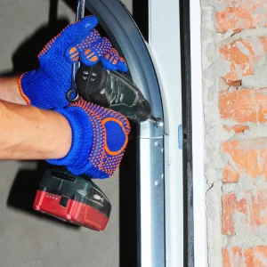 Technician wearing blue work gloves using a power drill to install or repair a garage door track