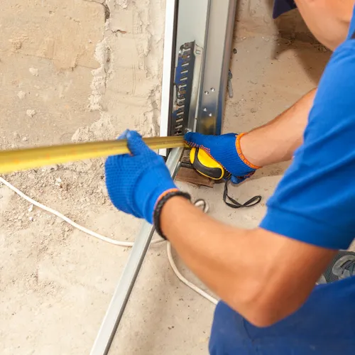 Technician in gloves using a tape measure to take precise measurements of a metal garage door track