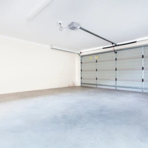 Empty, well-lit garage with a closed sectional garage door and a ceiling-mounted automatic opener system