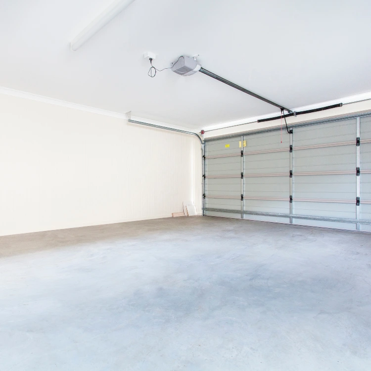 Empty, well-lit garage with a closed sectional garage door and a ceiling-mounted automatic opener system