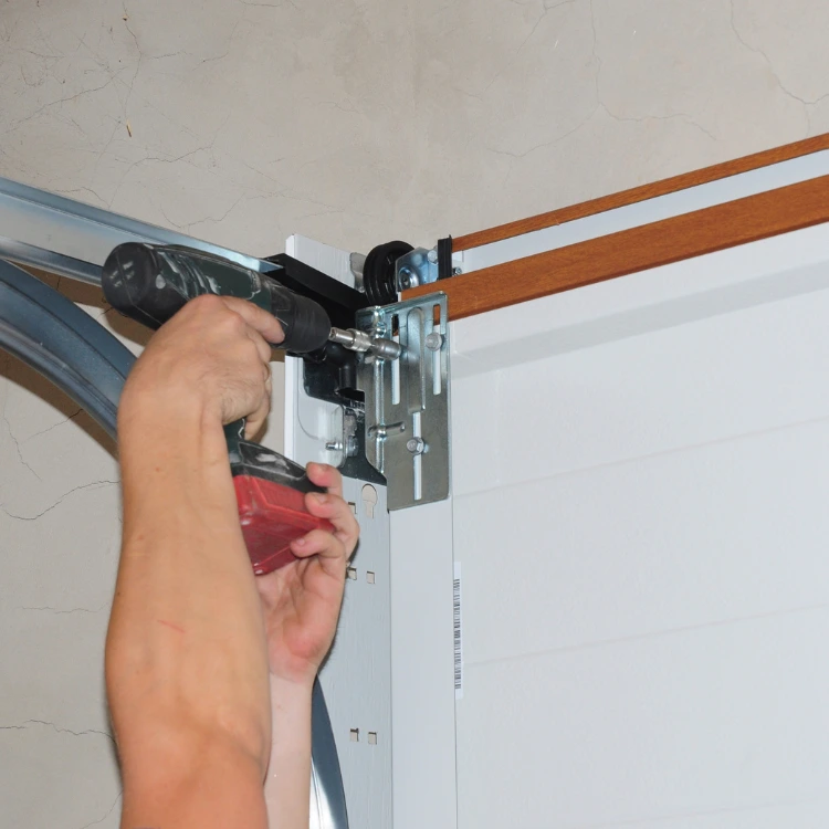 Close-up of a worker using a drill to secure hardware on a white garage door